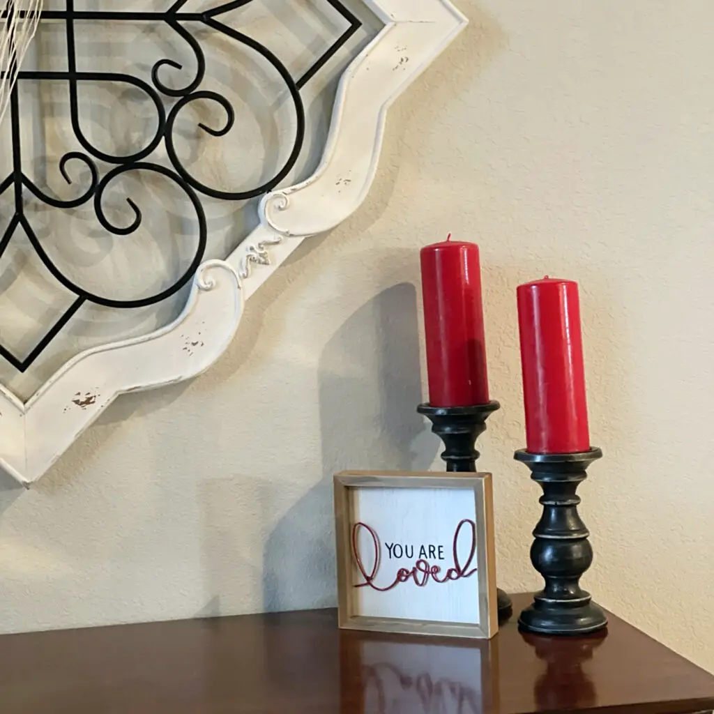Two black candlesticks with red candles and you are loved sign