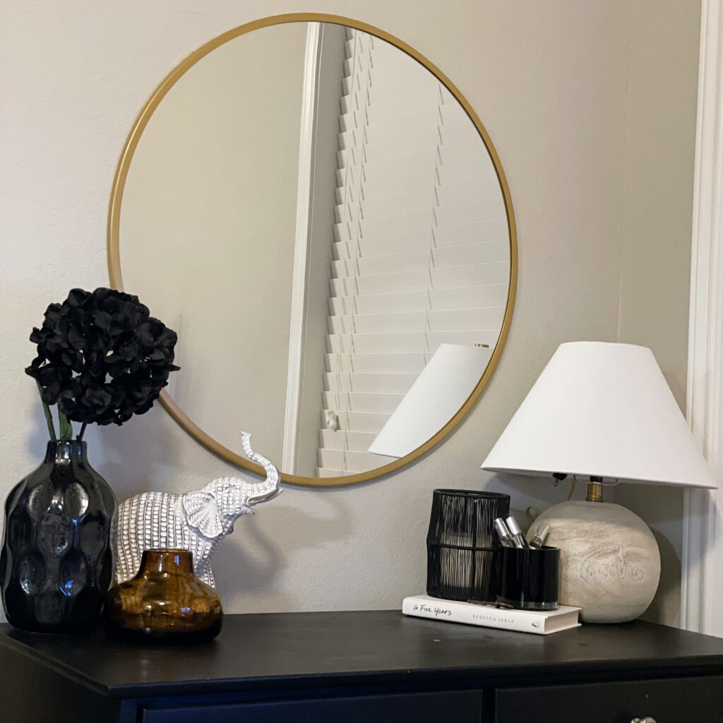 black vase and other black accents with a light, wooden lamp on top of bedroom dresser