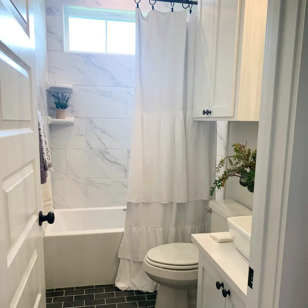 White ruffled shower curtain in all white bathroom with black tile