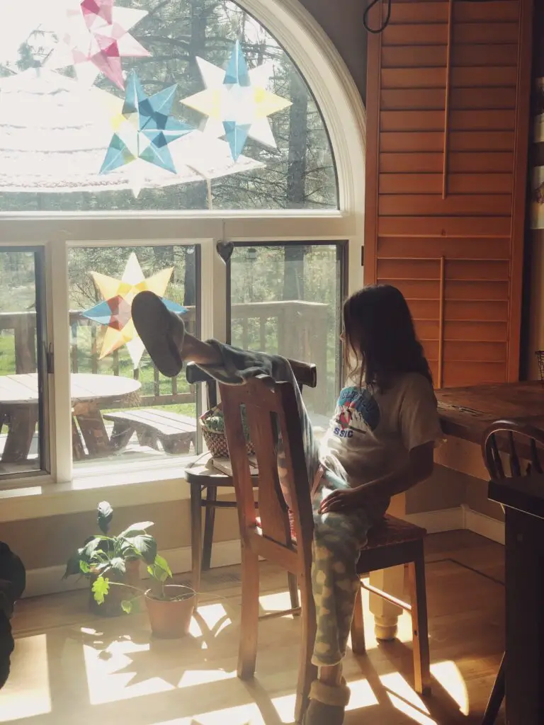 girl sitting backwards in chair looking out a big window that has paper stars glued to it