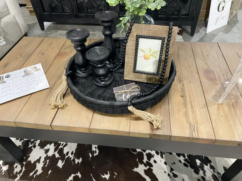 Black wicker tray, filled with wood accents, black decorations, and greenery on a rectangular coffee table