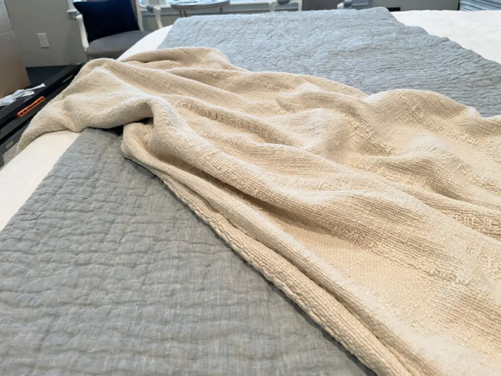 Chambray quilt on white bedding with beige throw blanket draped on top