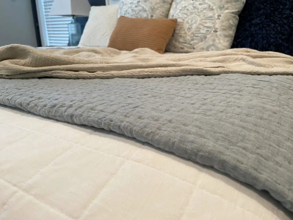 Chambray quilt, beige blanket, and patterned throw pillows. 