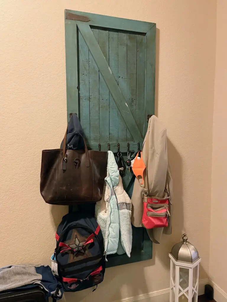 antique, teal door transformed into decor with metal hooks holding every day items such as bags, keys, and jackets