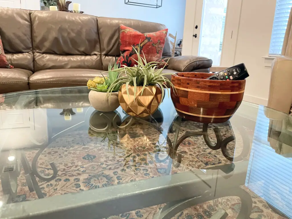 Glass coffee table decorated with wooden bowl & small succulents
