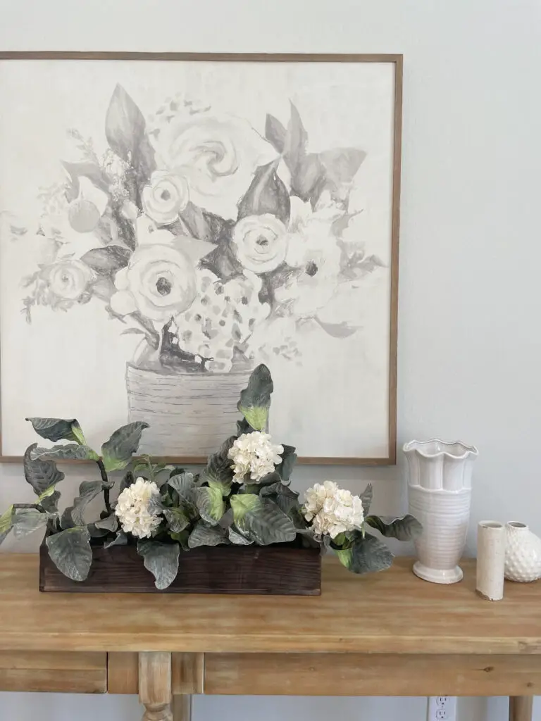 grey and white floral painting behind decorated side tableTake