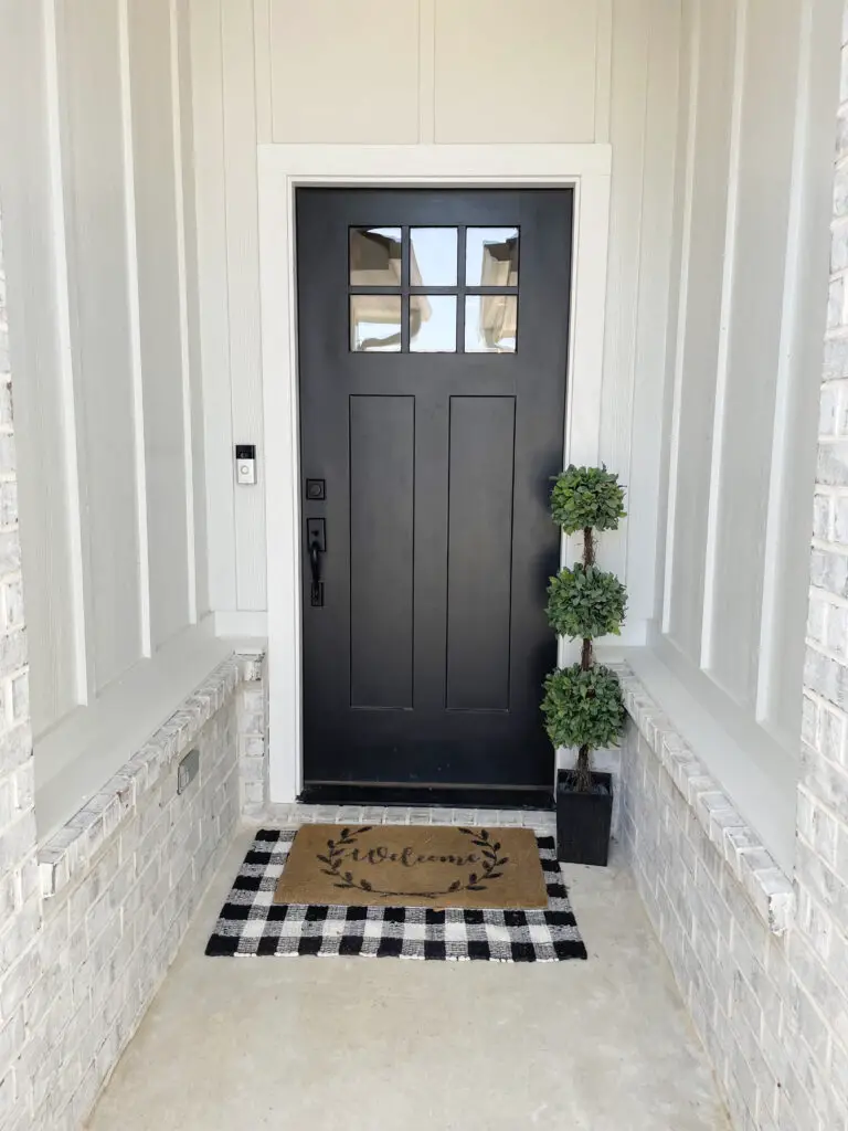 Black and white checkered rug layered under a brown welcome mat in front of black door