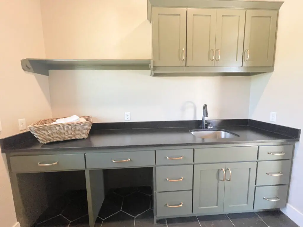 Mossy green laundry room cabinets with black countertops in laundry room
