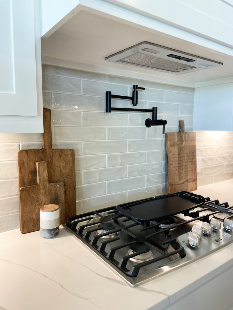 Wooden cutting boards laid on countertop framing a black stove and pot filler in a glorious white kitchen