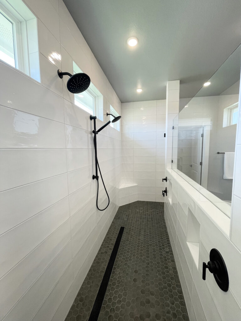 Giant walk in shower with white tile walls and a dark hexagon flooring
