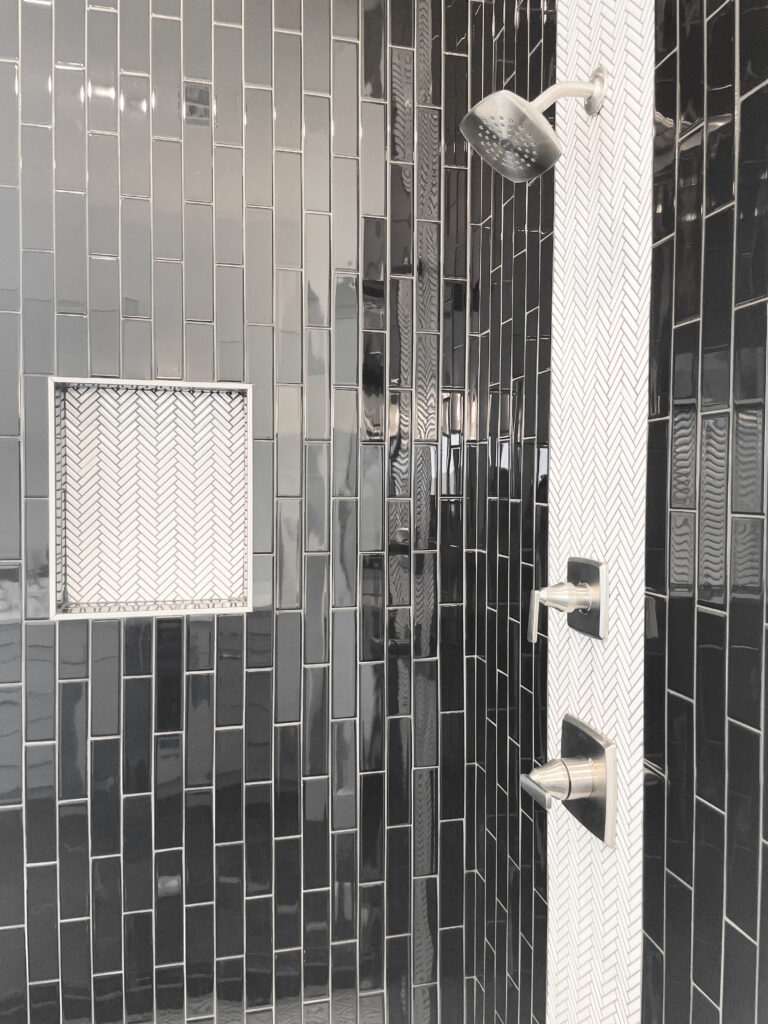 Black subway tile laid vertically with small white chevron tile accents