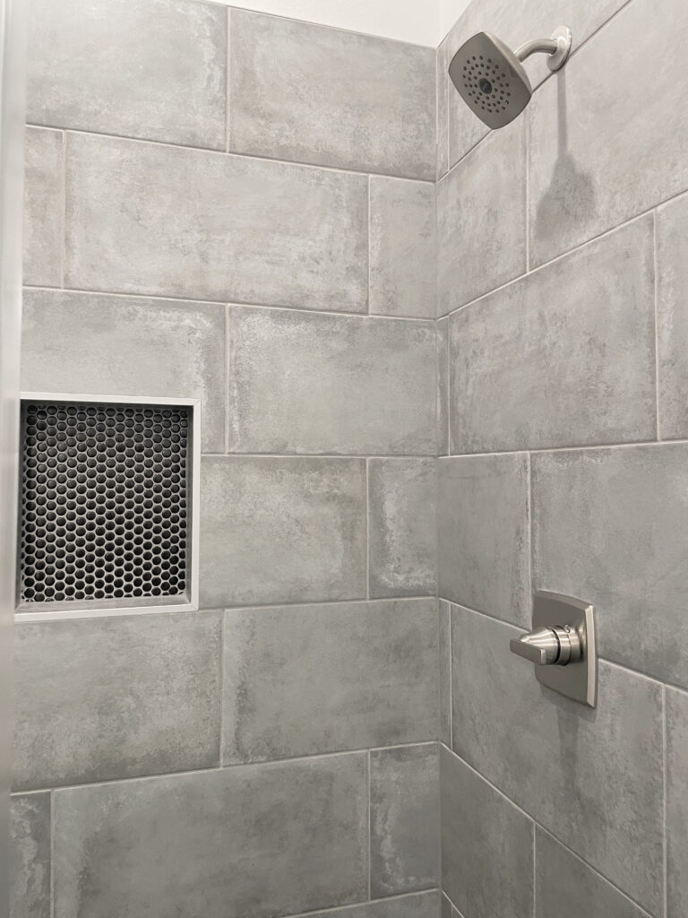 Large, grey, shower tile with a concrete look and a black penny soap cut out