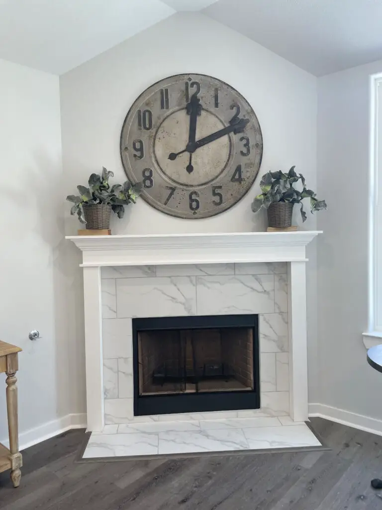 White fireplace with rustic clock framed by two plants on the mantle
