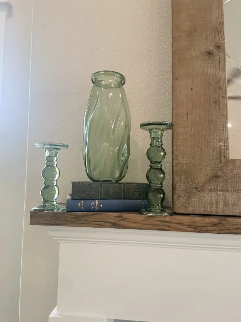 Green glass vase and candlesticks stacked on top of a couple of books on a fireplace mantle