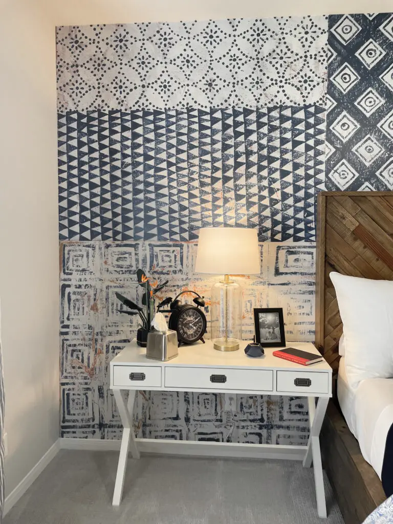 White bedside table that looks like a desk with modern and industrial accents on top against a blue patterned wallpaper