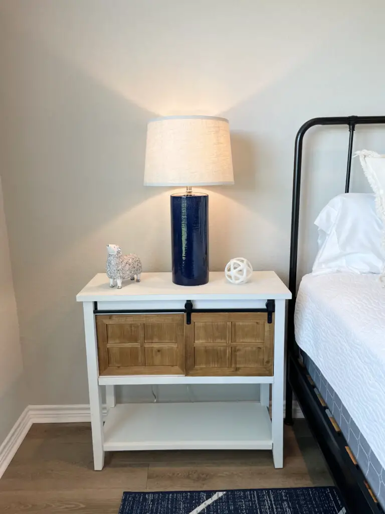 White nightstand next to iron bed frame with fun blue, white and grey accents