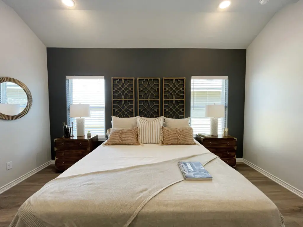 Dark grey accent wall, with light linen colors and wooden dressers as nightstands on either side of the bed