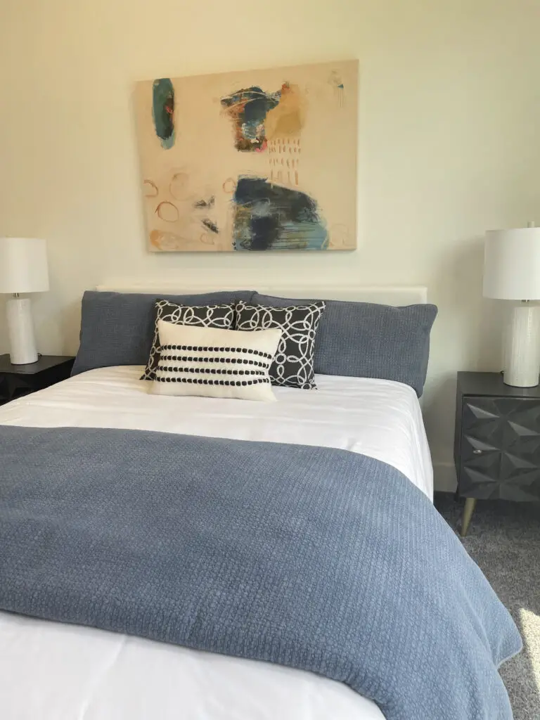 Black mid-century modern bedside tables next to a white leather headboard with blue bedding