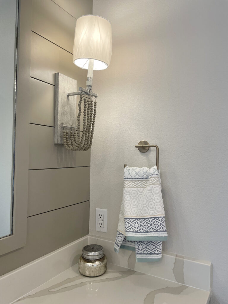 Grey ship la wall with beaded sconce base and textured shade placed next to coastal bathroom decor