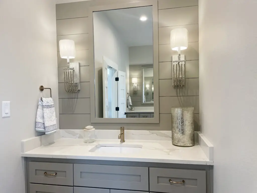 Grey bathroom vanity with coastal accents and beaded wall sconces on either side of the vanity mirror