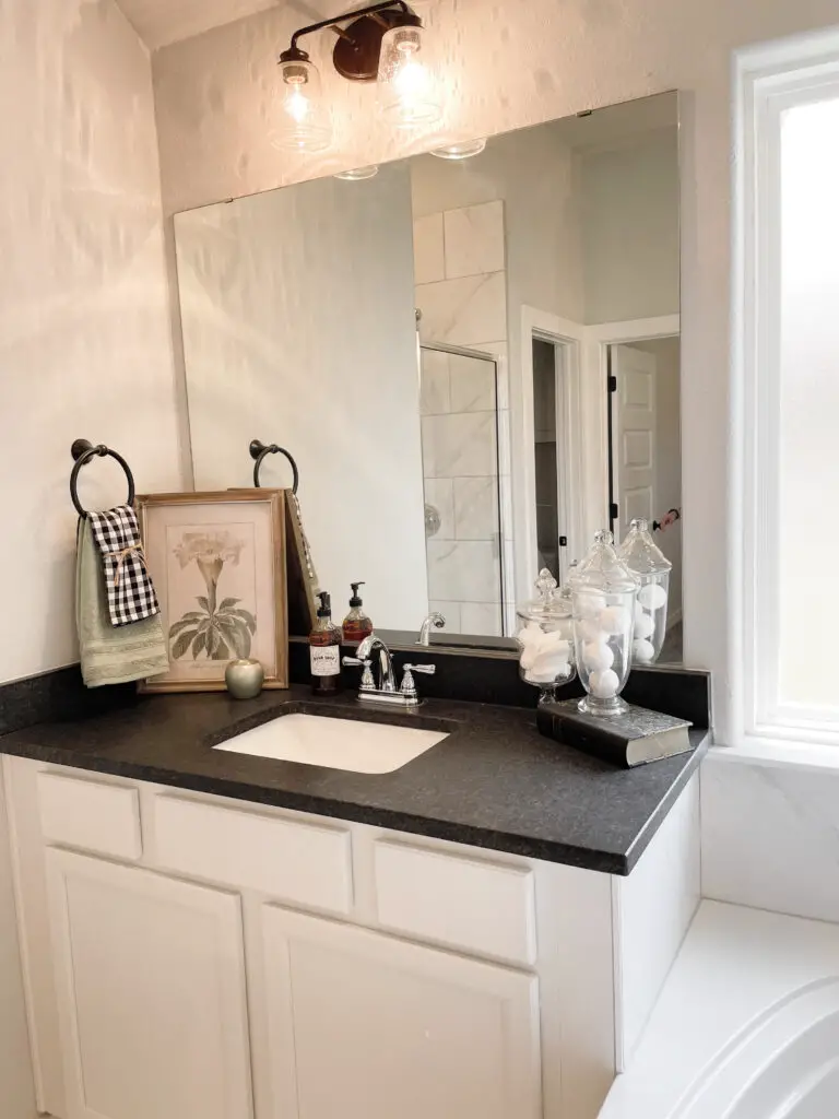 Black and white vanity with green, white, and black decorations such as a picture, towels, and soap dispenser