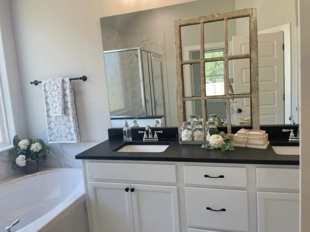 Double vanity with black counters and chick farmhouse accents such as stacked books, flowers, mason jars, and soap dispensers