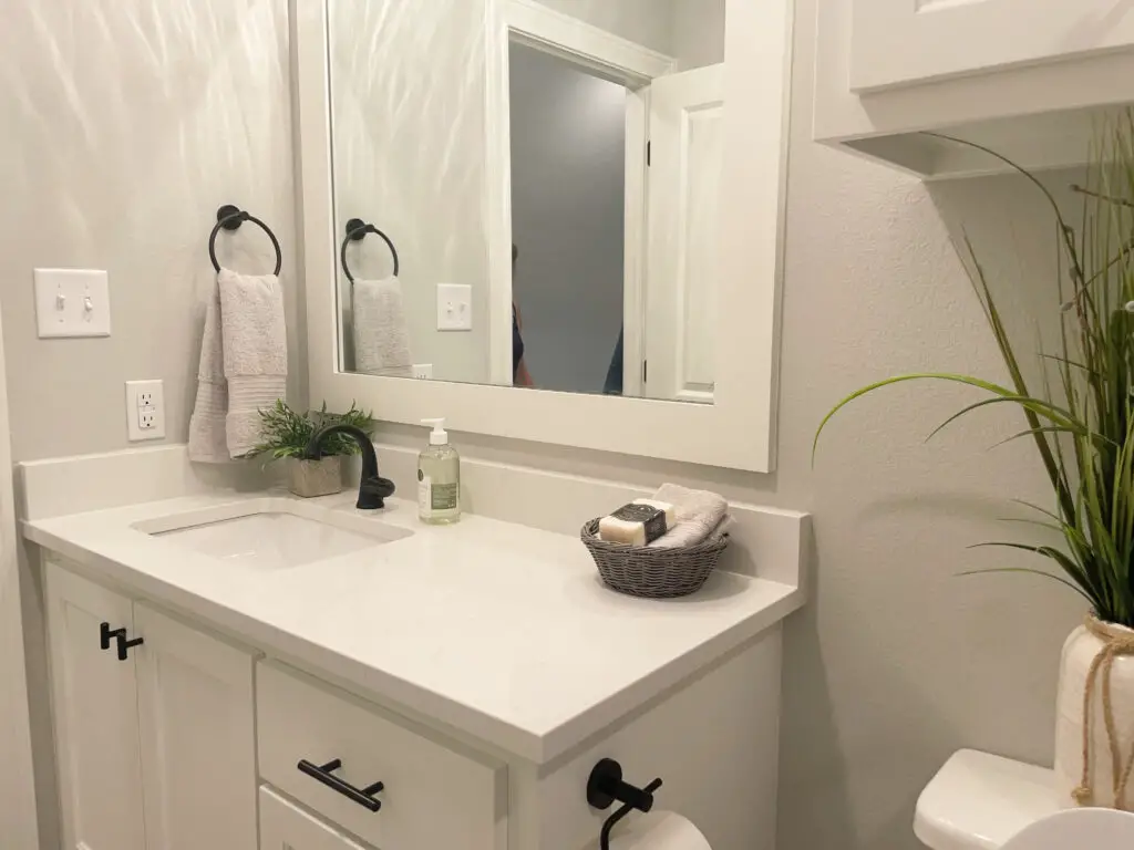 White bathroom with plant, soap dispenser, and grey wicker basket filled with towels and soap