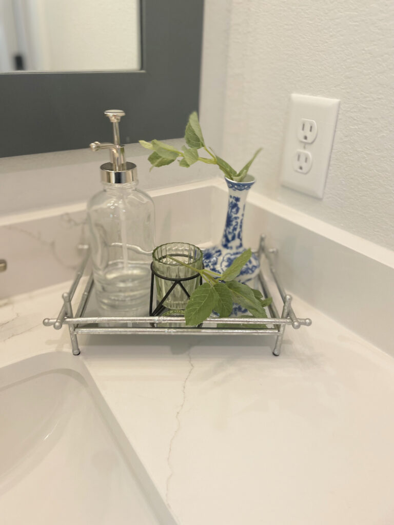 chic silver tray with soap dispenser, candle holder and blue and white vase with greenery on vanity
