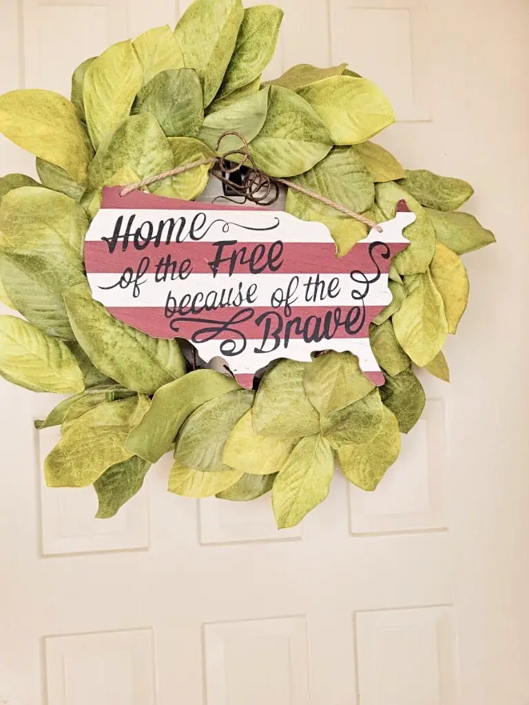 Green leaf wreath with America shaped wood with red and white stripes and cursive wording