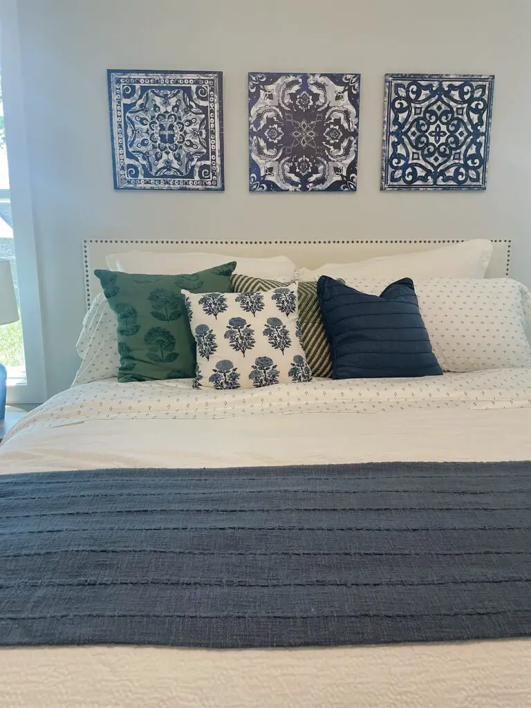 White headboard with studding around the edge and blue, white and green bed linens and throw pillows