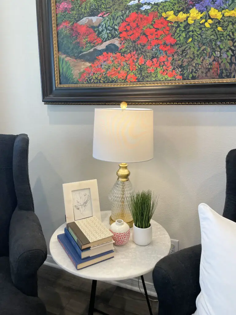 Pops of colored accents such as books, vases, plants, picture frame and lamp positioned quaintly on a marble top side table