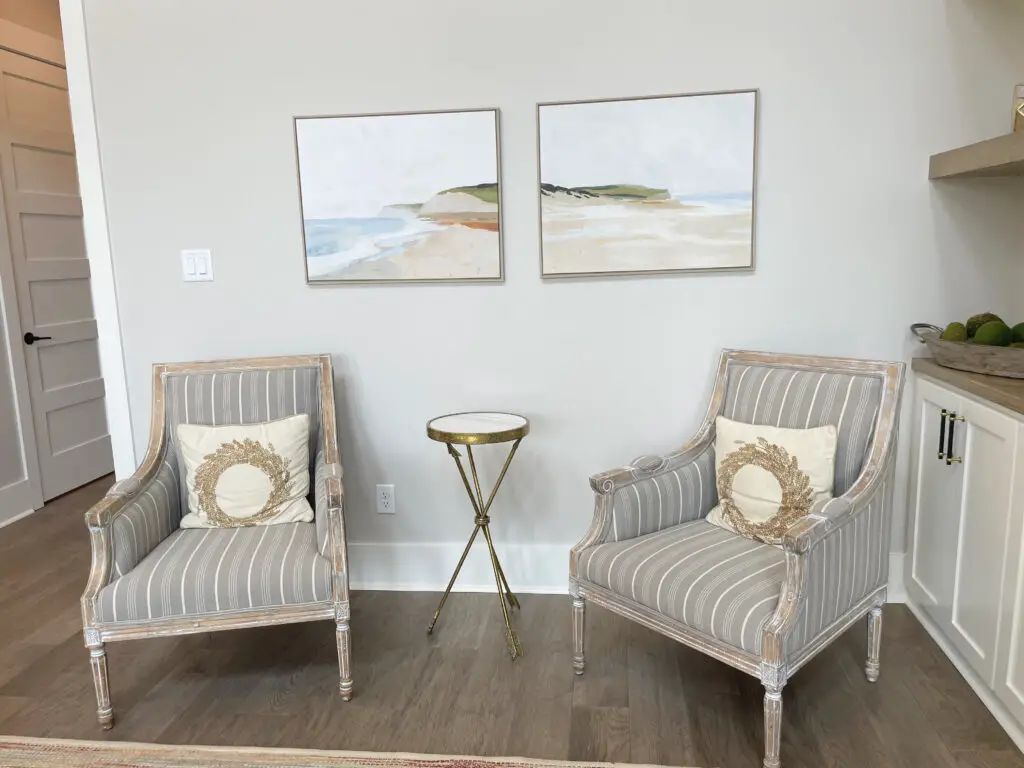 white washed chairs with grey upholstery and gold and white side table under two painted canvas art pieces