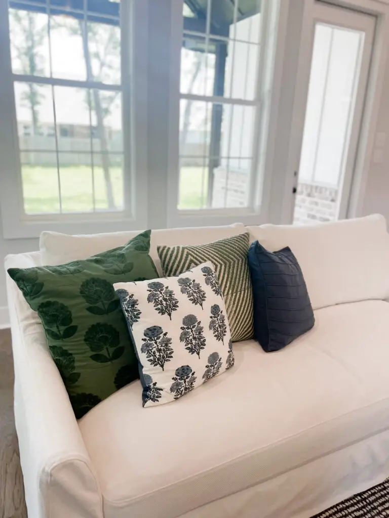 Green, white, and blue pillows with various patterns and textures on a white sofa
