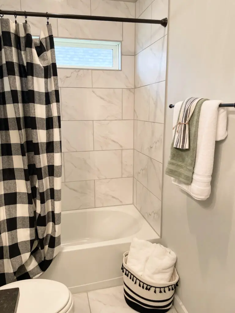 Black and white rope basket with two large white towels rolled up next to the shower