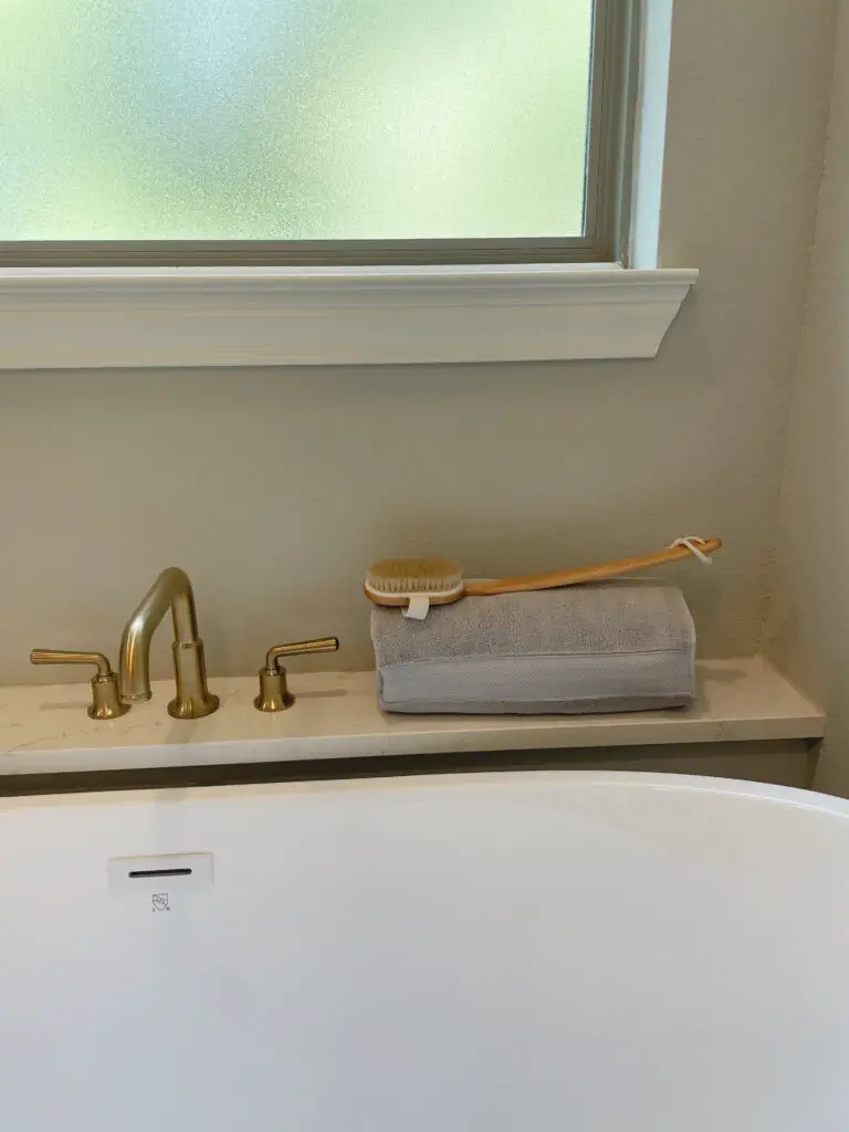 Grey towel folded on the ledge behind the bathtub with a back scratcher on top