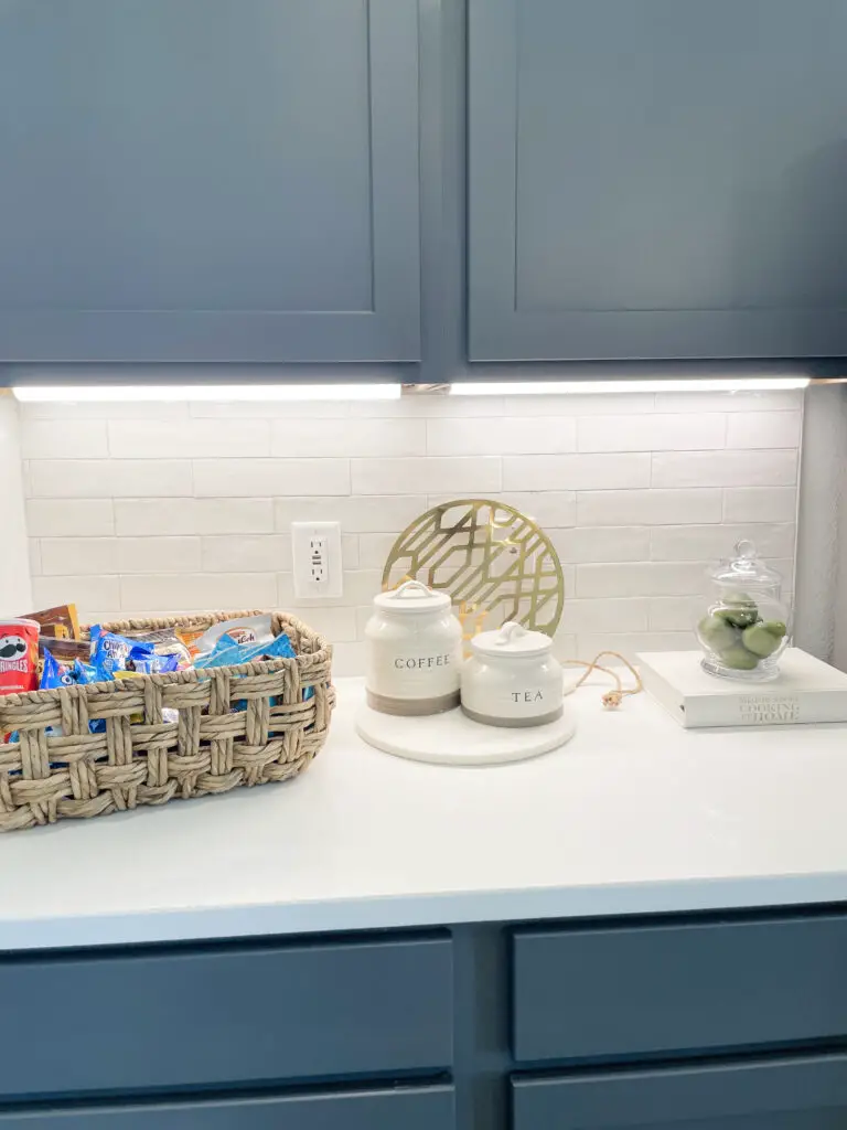 Wicker basket on kitchen island filled with snacks and surrounded by white and gold accents