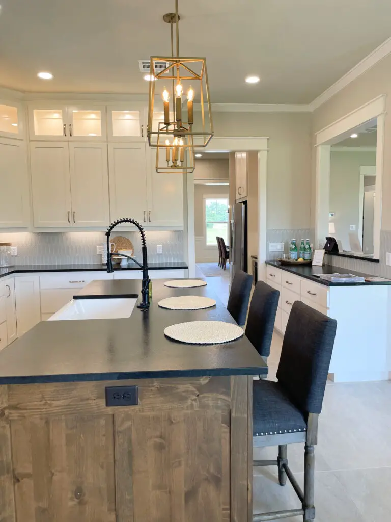 Grey fabric stools with brown legs in a white kitchen with a medium brown wood island and black countertops