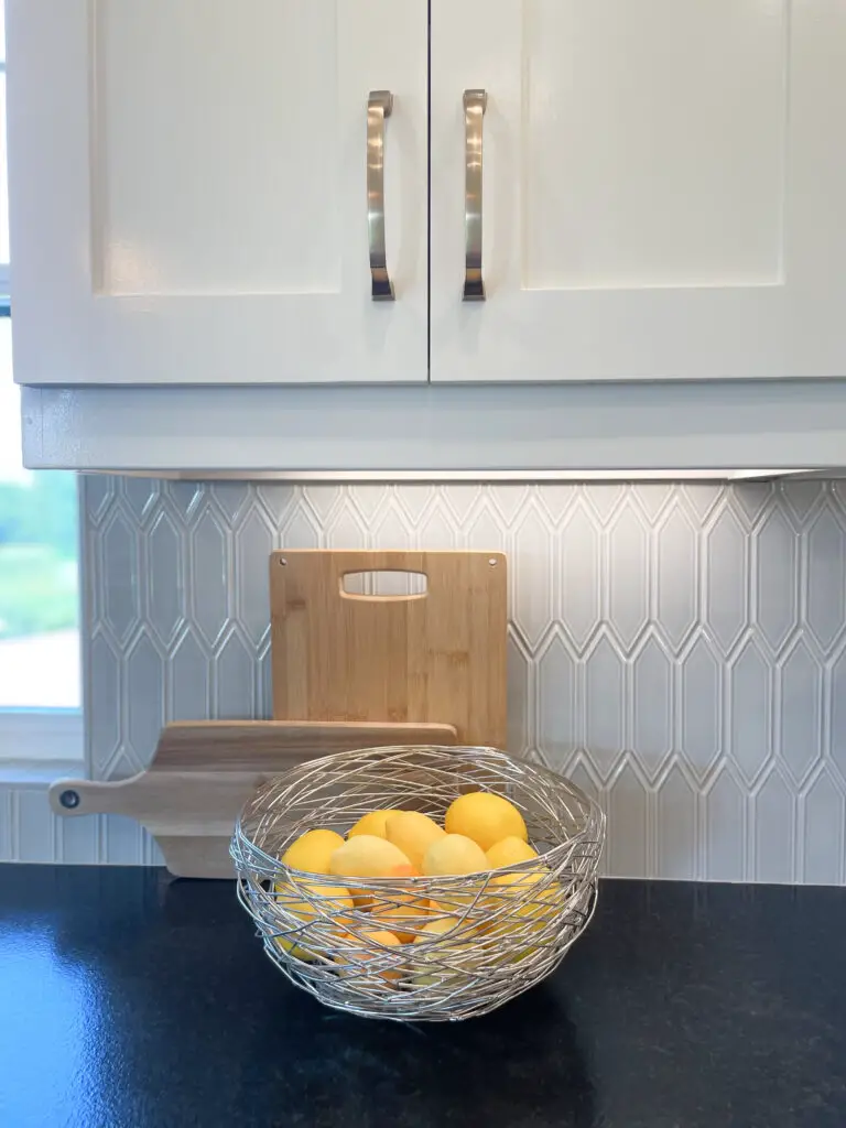 Silver bowl with lemons in front of two cutting boards splayed in different directions propped against white kitchen backsplash in a put together design