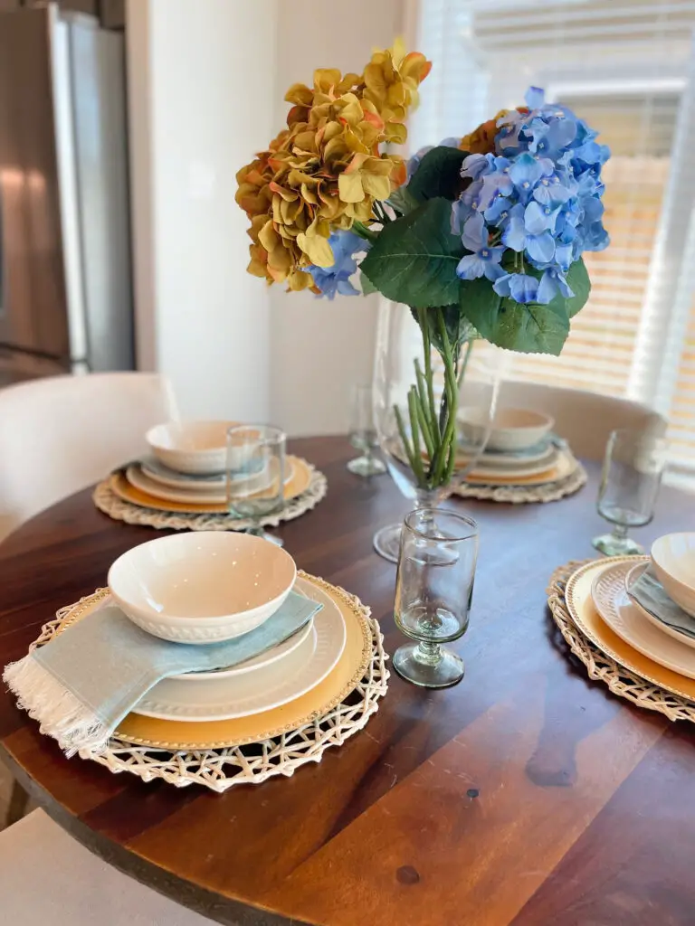 White dishes on a gold charger and wicker placemat with clear, stemmed glasses on round table