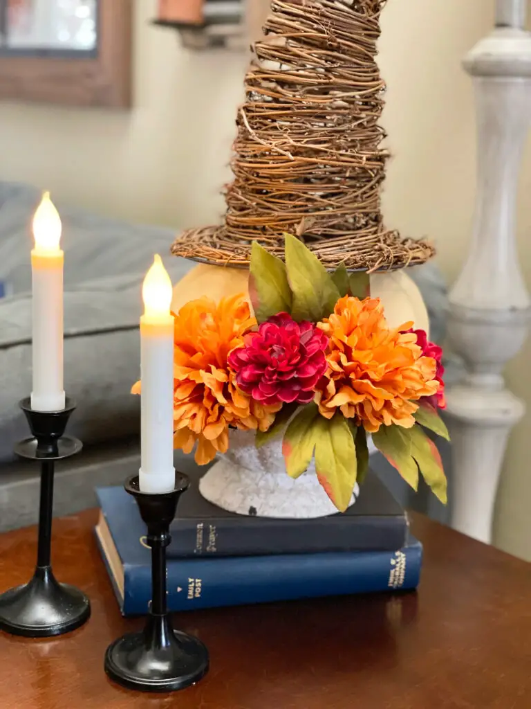 Bowl stacked on books with pumpkins wearing twine witches hat surrounded by candlesticks