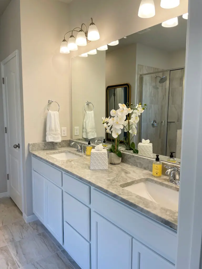 Grey counter with thick veining and white cabinets on dual vanity with yellow and white decorative accents in master bathroom