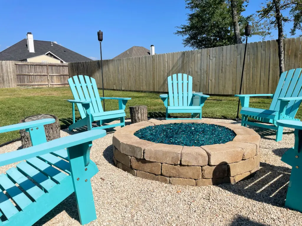 Stone fire pit with teal rocks and Adirondack chairs