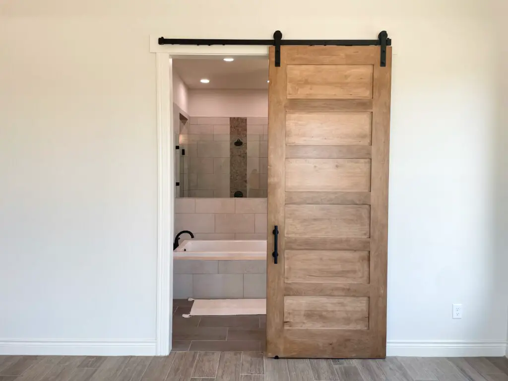 Timeless medium brown barn door with matte black hardware into master bathroom