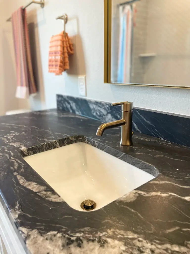Black marble counter in bathroom with modern brass faucet and mirror