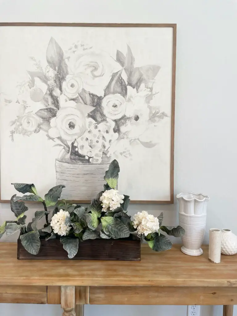 Dark wood box with white floral arrangement next to white vases and farmhouse painting