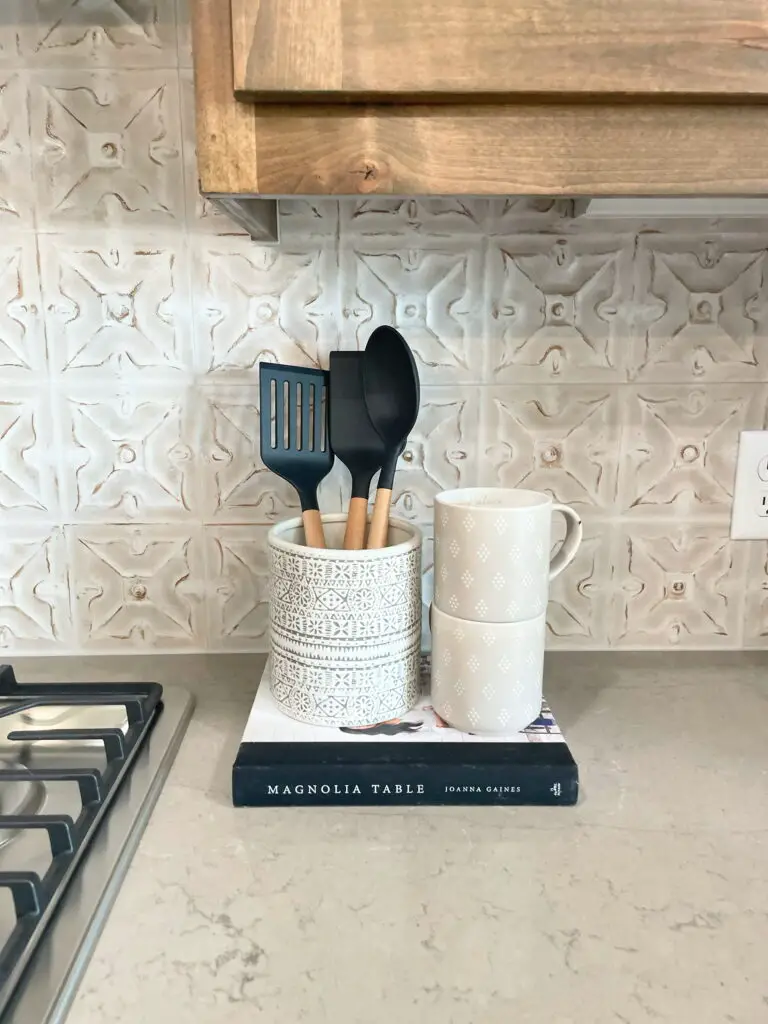 stacked coffee mugs next to utensil holder on top of book
