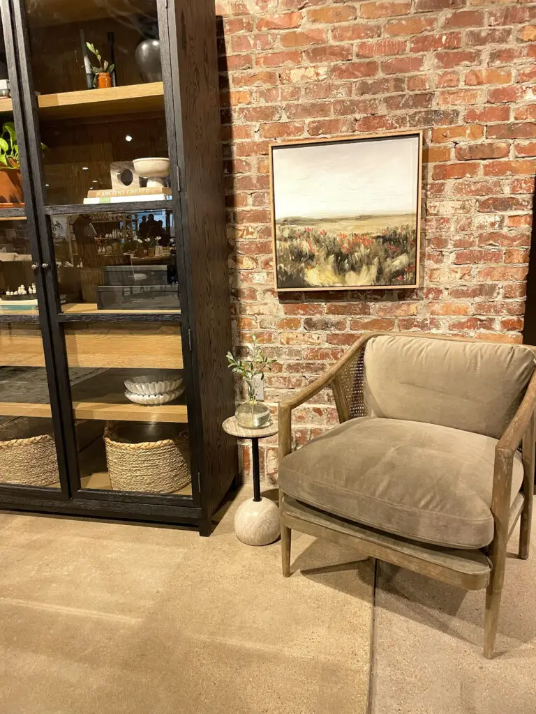 Cane accent chair with small side table underneath a landscape painting